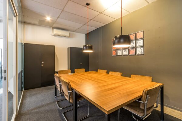 Vergaderruimte aan de Jan van Eycklaan met een houten tafel, leren stoelen en twee hanglampen.